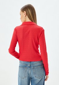 Rød, struktureret skjorte med lange ærmer og krave, parret med høj talje blå denim jeans; har en slank silhuet og afslappet design.