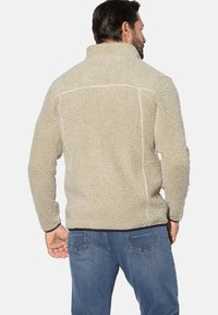 Beige fleece jacket with a high collar and textured surface. Features a solid color and contrast stitching along the seams.