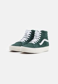 Sapatilhas altas em camurça verde escuro com atacadores brancos. Apresentam um logo em forma de onda branco, costuras em contraste e uma sola de borracha branca sólida.