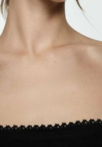 Vêtement noir avec une bordure en dentelle festonnée au niveau de l'encolure, reposant juste en dessous de la clavicule. Peau lisse visible au-dessus du tissu.