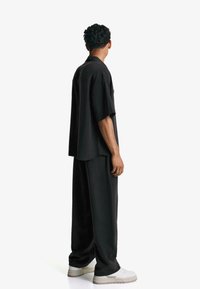 Black short-sleeve shirt with a relaxed fit, paired with loose black trousers. The outfit features a simple, minimalist design and a subtle texture.