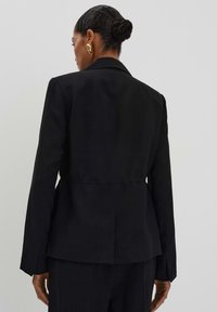 Zwarte blazer met een aangesloten taille, lange mouwen en een open rug. Glad materiaal met een klassieke gelaste kraag en een minimalistisch ontwerp.