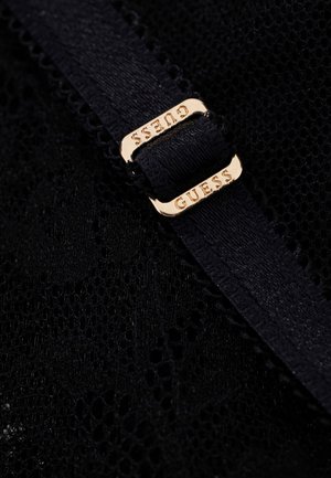 Schwarzer Spitzenstoff mit einem schwarzen elastischen Riemen, der durch eine goldene Metallschnalle mit eingraviertem Markennamen „GUESS“ geführt ist.