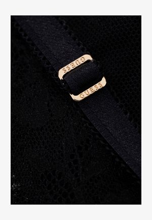 Tela de encaje negra con una banda elástica negra pasada por una hebilla metálica dorada grabada con el nombre de la marca "GUESS."