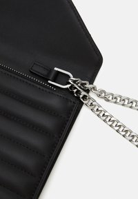 Czarna skórzana torba z pikowanym wzorem, srebrnym łańcuszkiem, zapięciem na zamek oraz gładką fakturą w minimalistycznym stylu.