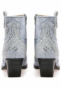Stivaletti in denim azzurro chiaro con borchie decorative argentate, chiusura con zip e tacco spesso nero. Presentano dettagli testurizzati nella parte superiore.