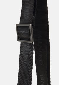 Cintura in nylon nera con una fibbia quadrata argentata. Presenta il logo "VALENTINO" in rilievo lungo la superficie della cintura, tessuto testurizzato.