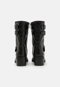 Czarne skórzane botki sięgające kostki z okrągłym noskiem, ozdobione trzema zapięciami na klamry, posiadające teksturowaną powierzchnię i niskie blokowe obcasy.