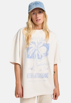 Light beige oversized t-shirt made of cotton, featuring a blue graphic of a palm tree and sun, with "BILLABONG" text at the bottom.