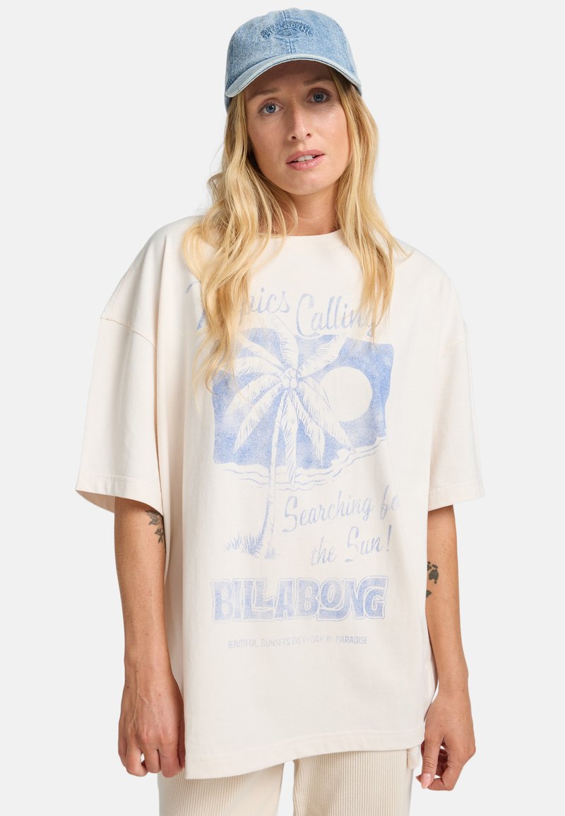 Lys beige oversized t-shirt lavet af bomuld, med et blåt grafik af et palmetræ og sol, med "BILLABONG" tekst nederst.