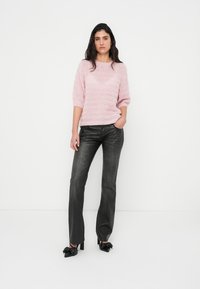 Απαλό ροζ πουλόβερ πλεκτό με κοντά μανίκια και υφή, συνδυασμένο με σκούρο γκρι παντελόνι που μοιάζει με δέρμα και μαύρα παπούτσια με τακούνι.