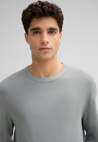 Helles graues Langarmshirt mit einem strukturierten, gerippten Muster und Rundhalsausschnitt. Der Stoff wirkt weich und lässig.