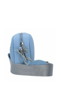 Borsa in pelle azzurra chiara con forma arrotondata, hardware in argento e una ampia tracolla grigia con branding in rilievo. Visibile dettaglio della chiusura con zip.