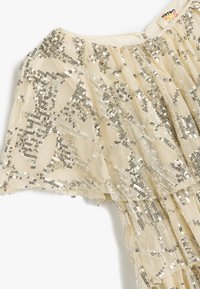 Beige paljettklänning med utsvängd kort ärm, lagerdesign och glänsande silverpaljetter ordnade i ett geometriskt mönster på genomskinligt tyg.