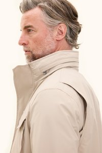 Beige waterdichte jas met hoge kraag, knopen sluiting aan de voorkant en zijzak. Glad oppervlak en gestructureerd ontwerp.