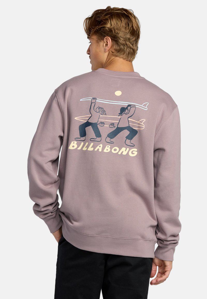 Purple sweatshirt with a crew neck, featuring a graphic of two figures carrying a surfboard, and the text "BILLABONG" in yellow.