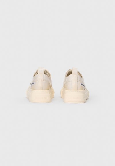 Zapatillas de color crema con una textura suave, que cuentan con una suela gruesa y una cinta trasera. Marca destacada en los laterales.