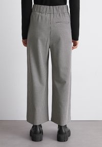 Schwarz-weiße Hahnentrittmusterweite Hose mit elastischem Bund, versehen mit einer hinteren Tasche und getragen mit klobigen schwarzen Stiefeln.