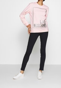 Pink sweatshirt with "LOVE MOSCHINO" in black glitter, paired with black skinny jeans and white sneakers. Long sleeves and round neckline.