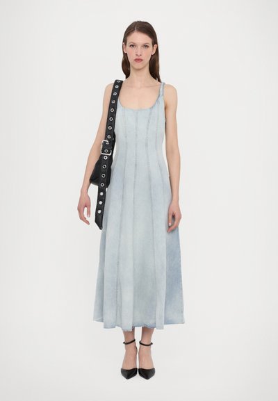 Denim-Midikleid in Hellblau, mit tailliertem Oberteil, geradem Schnitt und Seitennähten. Kombiniert mit einer schwarzen Schultertasche und spitzen Pumps.