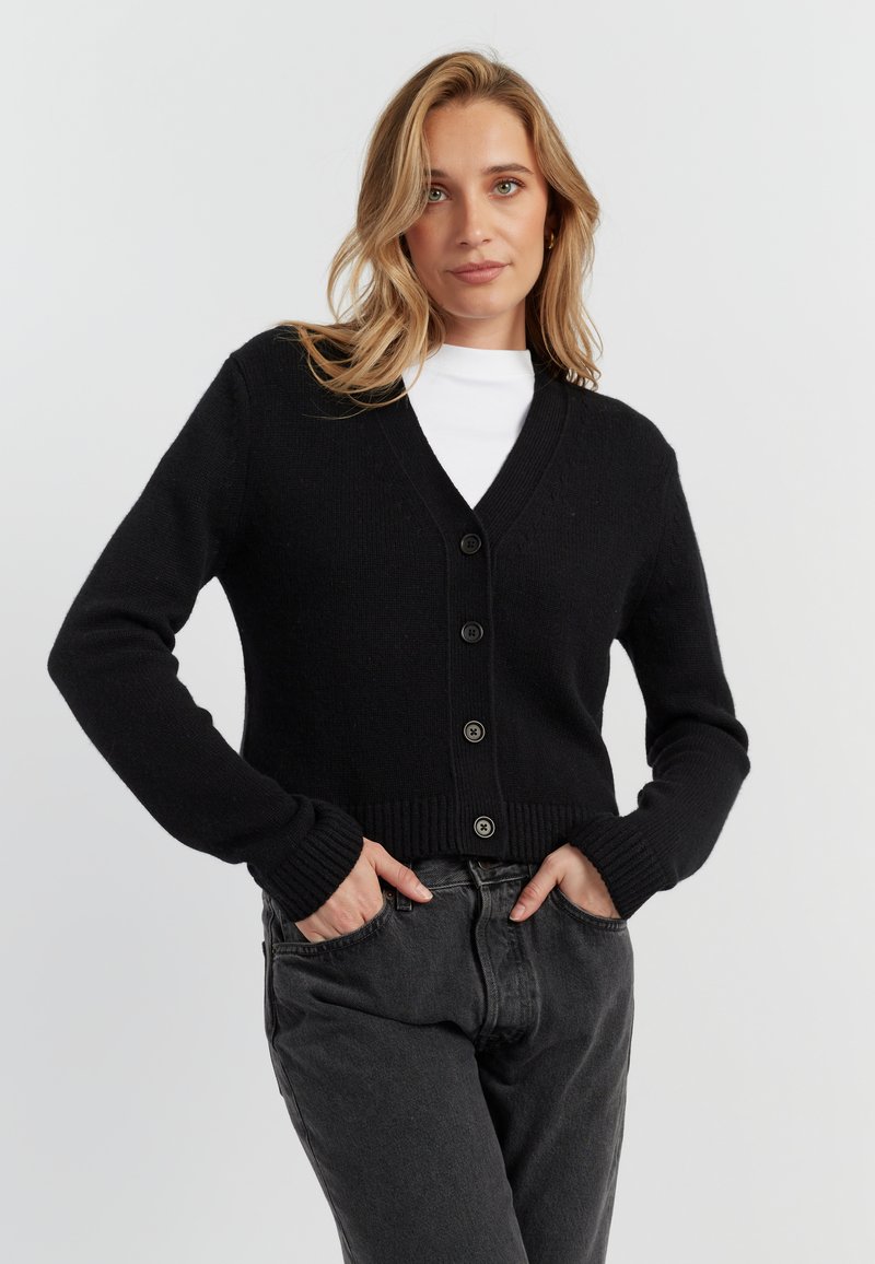 Cardigan nero realizzato in tessuto a maglia testurizzato, con scollo a V, chiusura con bottoni e polsini e orlo a coste. Abbinato a jeans grigio scuro.