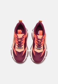 Sport sneakers i mørke lilla og ferskenfarvet med netpaneler, tyk hvid mellemsål og kontrastfarvede snørebånd. Tekstureret overflade, dristigt design.