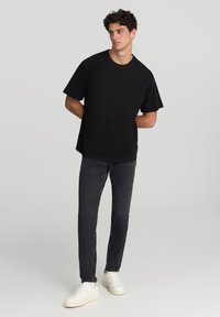 T-shirt nera a maniche corte con vestibilità ampia, abbinata a jeans in denim scuro e sneaker bianche. Design semplice, senza motivi o grafiche visibili.