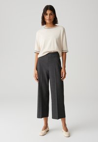 Beige T-shirt met korte mouwen en zwarte afwerking, gecombineerd met donker gecontroleerde wijde broek en nude instappers. Eenvoudig ontwerp, comfortabele pasvorm.