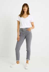 Vaqueros grises de talle alto con una forma ajustada, detalle de botones y bolsillos laterales, combinados con una camiseta blanca de cuello en V y zapatillas blancas.