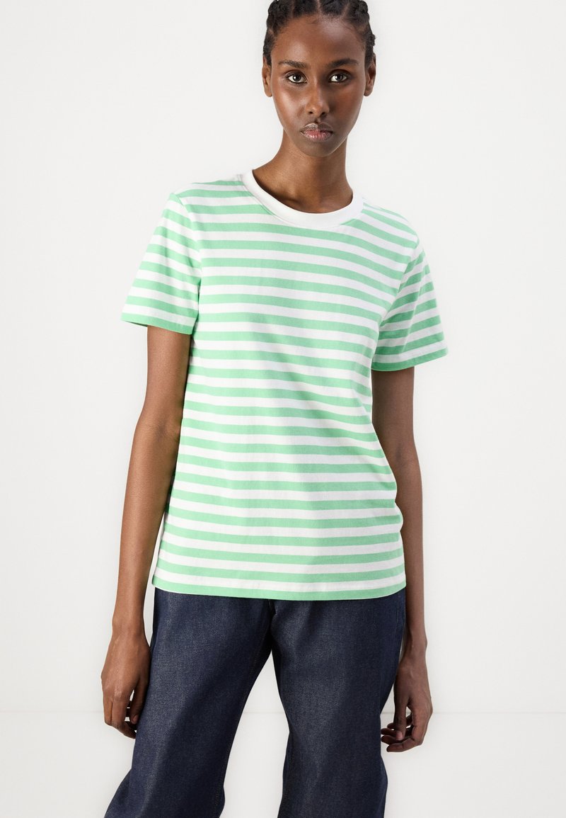 Camiseta de manga corta a rayas verdes y blancas con cuello redondo, hecha de suave tela de algodón, combinada con pantalones de mezclilla oscuros.