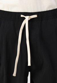 Sorte shorts med snøre i livet, med en cremefarvet snøre. Materialet ser letvægtigt ud med en glat tekstur.