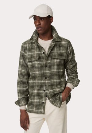 Zielona koszula w kratę z flaneli, z kołnierzykiem, zapinana na guziki, mająca dwie kieszenie na piersi. Nosi się ją na jasnym swetrze, z jasnymi spodniami.