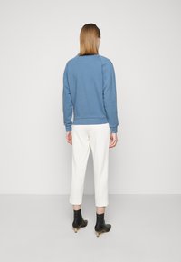 Sweat-shirt bleu clair vu de dos, avec un col rond et des poignets côtelés, associé à un pantalon blanc fuselé et des bottines noires.