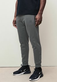 Graue Sweatpants aus weichem Stoff, mit dezentem Logo am linken Oberschenkel, schlanker Schnitt, kontrastierenden Nähten und gerippten Bündchen.