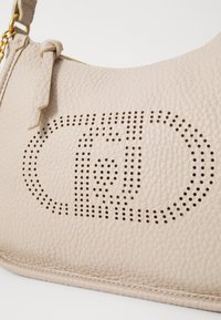 Bolso de mano de cuero beige con un diseño de logo perforado, superficie texturizada y cierre de cremallera con una correa de cadena.