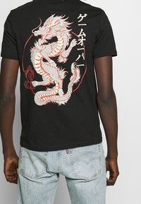 Czarny bawełniany t-shirt z dużą, kolorową grafiką smoka na plecach, ozdobioną czerwonymi konturami i japońskim tekstem.