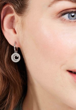 Silberfarbene, runde Ohrringe mit einem ausschnittlastigen Design. Die Ohrringe sind an einem Hoop befestigt und zeigen eine elegante, moderne Ästhetik.