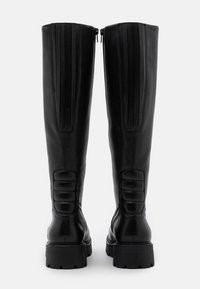 Botas de cuero negras hasta la rodilla con un acabado liso, que presentan cremalleras verticales prominentes y acentos acolchados en los lados. Suelas de goma gruesa.