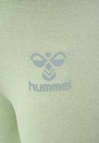 Ljusgrön sportklädesfabric med en slät textur, med en logotypdesign i en kontrasterande nyans. Varumärket "hummel" ingår.