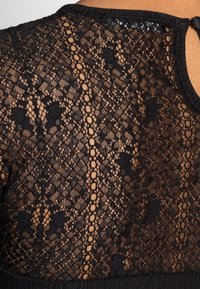 Top in pizzo nero con intricate fantasie, un design testurizzato, scollatura arrotondata e una piccola apertura a chiave sul retro.