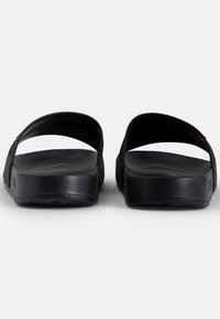 Mustat liukujalkineet, jotka on valmistettu teksturoidusta kumista. Varustettu leveällä hihnalla ja paksulla pohjalla, joka tarjoaa tasaisen ja pehmeän jalkatuen.