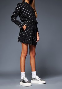 Vestido negro con patrones de lunas crecientes blancas, mangas largas y cintura elástica, combinado con zapatillas plateadas y calcetines tobilleros blancos.
