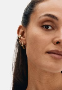 Gouden creolen in verschillende maten, met een gladde, glanzende afwerking en een minimalistisch ontwerp, gedragen aan het oor van het model.