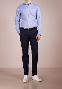 Camicia blu chiaro a maniche lunghe con colletto classico, cintura nera, pantaloni blu navy e sneakers bianche.
