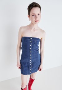 Mørkeblå denim stroppeløs kjole med en figursydd silhuett, med frontmetallknapper og en jevn tekstur. Stylet med røde knelang støvler.