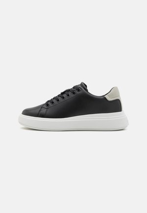 Black leather sneaker with round toe, white rubber sole, five eyelets for laces, and a gray heel accent. Smooth texture throughout.