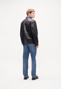 Black leather jacket with a classic collar, back yoke detail, and button cuffs, paired with light blue straight-leg jeans and black shoes.
