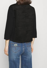 Top in suede nero con maniche a tre quarti, abbinato a jeans blu con logo "Lois" sulla tasca posteriore. Vestibilità casual.