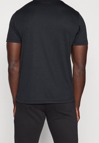 Czarny krótki rękaw t-shirt wykonany z gładkiego materiału. Posiada prosty krój, okrągły dekolt oraz widoczne szwy na dole i rękawach.