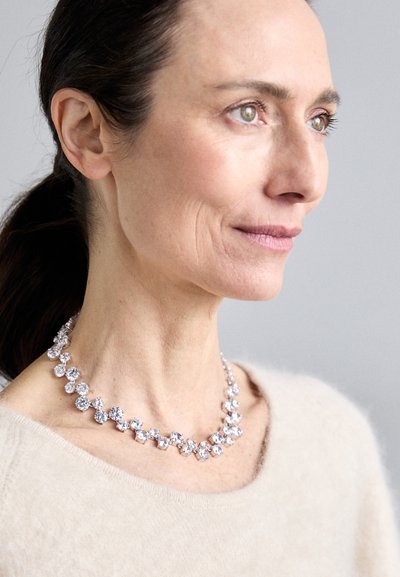 Collier en cristal présentant des pierres rondes et étincelantes disposées selon un motif dégradé, associé à un doux pull beige.